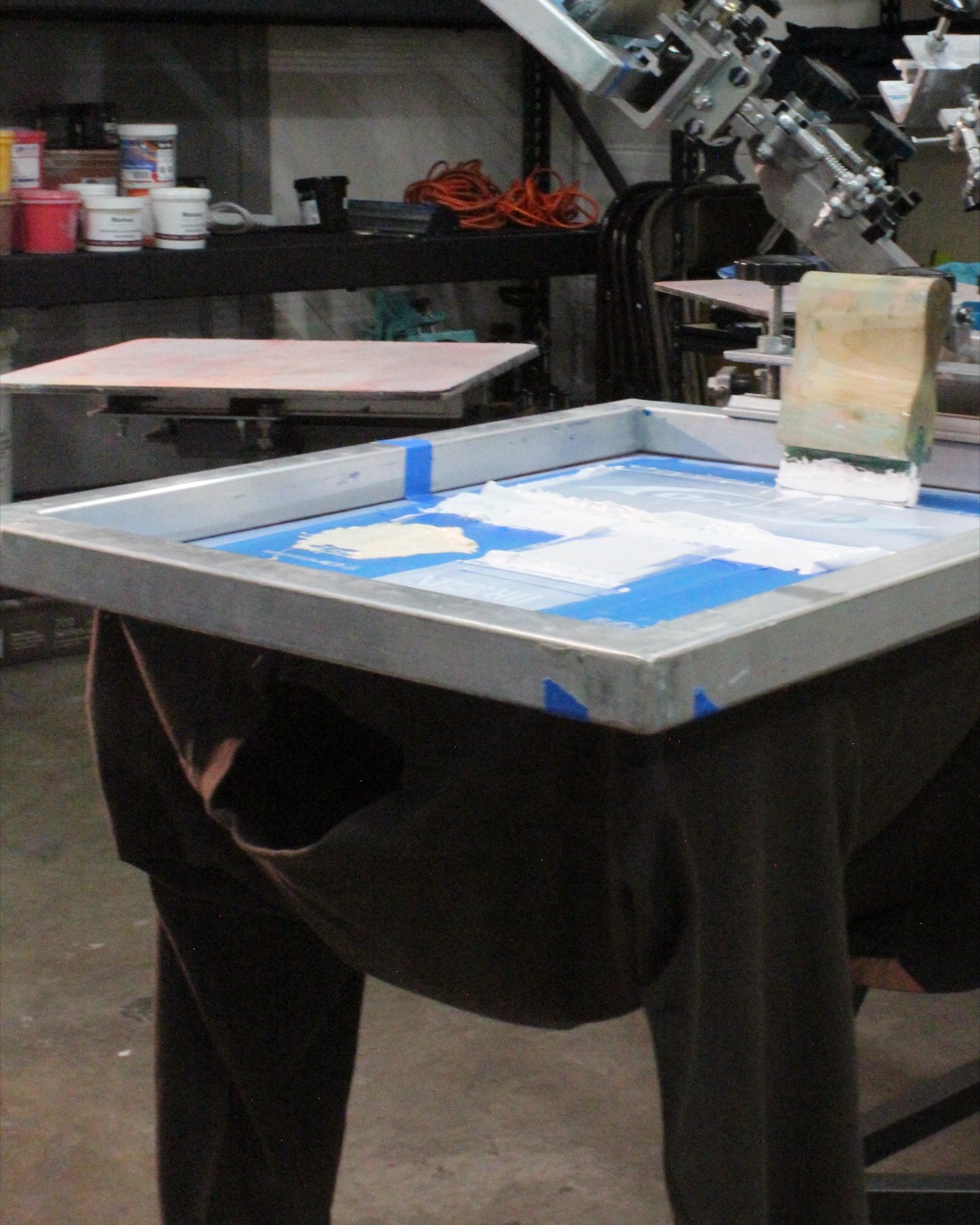 Screen printing press at the YD Print Pros shop, loaded screen and squeegee ready to pull